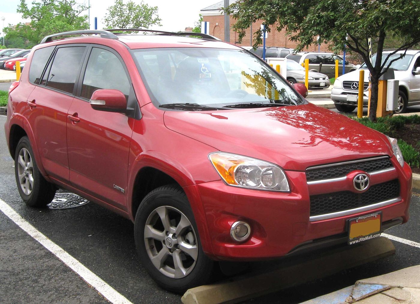A red compact SUV parked in a lot, seen from the front three-quarter angle, with trees behind it.