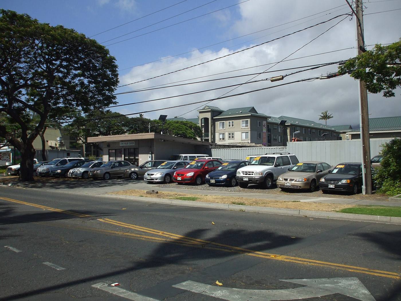 A wide view of a used car lot with rows of parked cars beside a street on a sunny day.