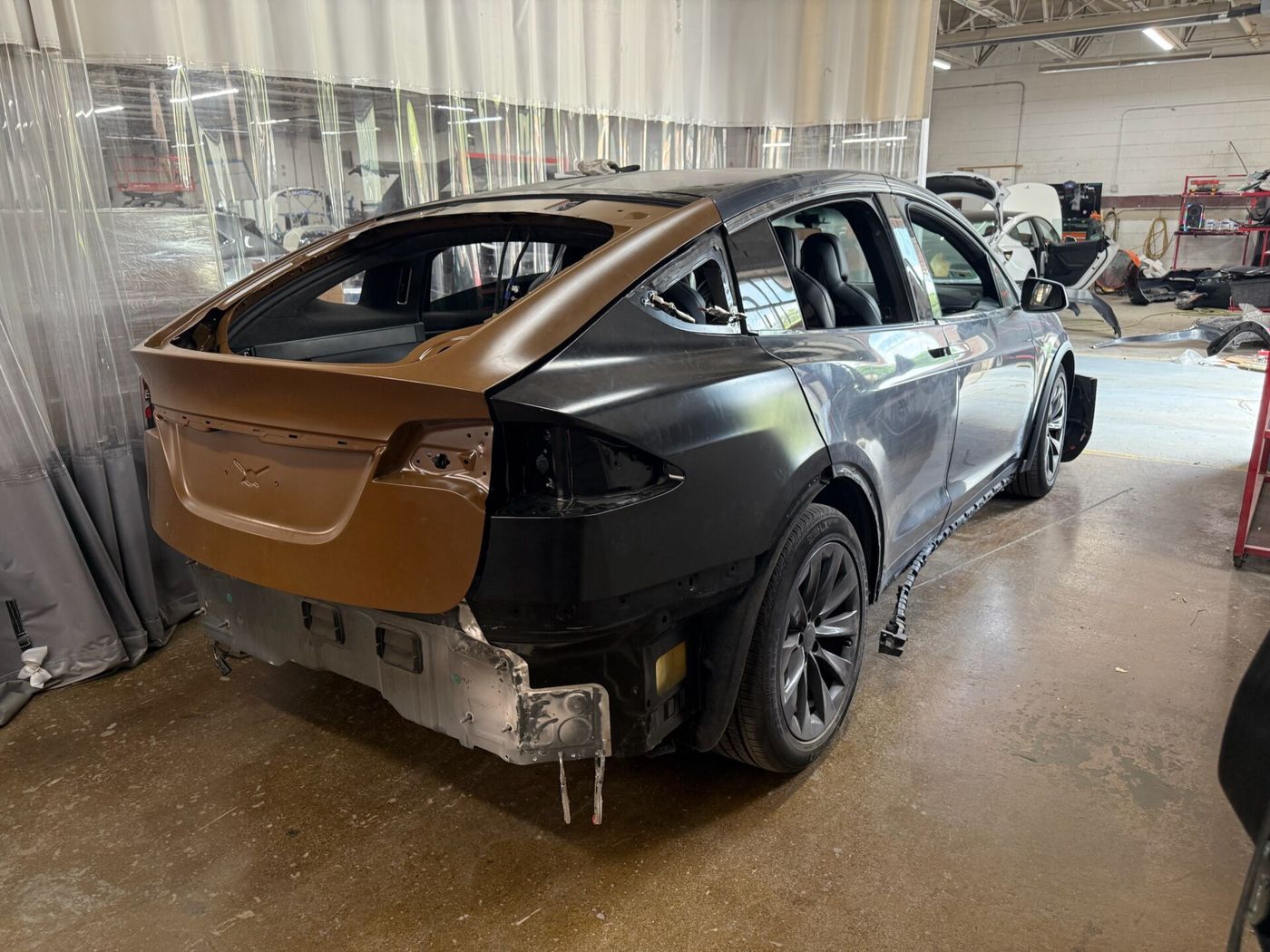 A grey SUV in a repair bay with its rear panels stripped back to bare metal and primer.